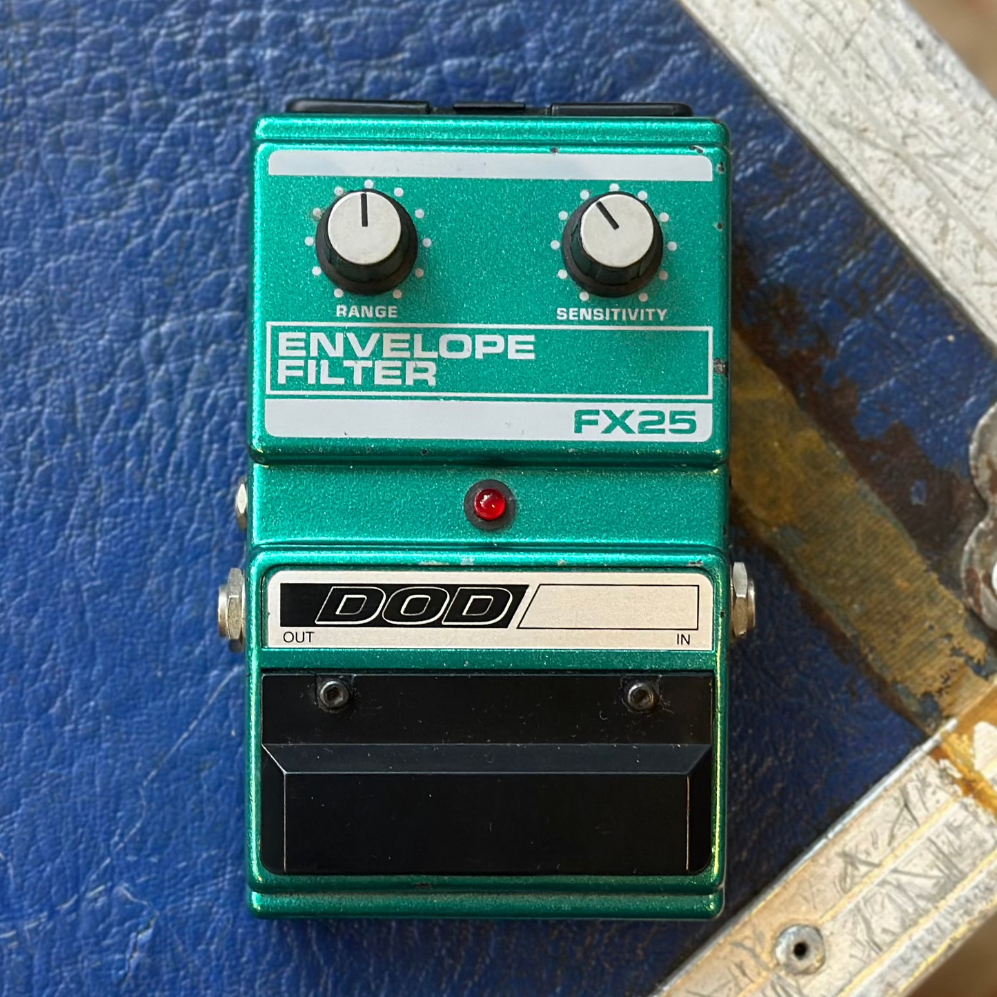 A green DOD FX25 Envelope Filter guitar pedal with black knobs and a black footswitch, resting on a textured blue equipment case.