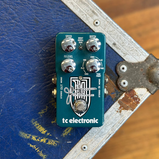 A TC Electronic Flanger guitar effects pedal with a teal green body and silver knobs, resting on a blue equipment case with a wooden floor visible in the background.