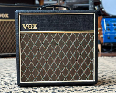 VOX guitar amplifier on a rug with musical instruments in the background